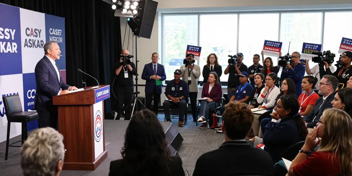 Casey Askar debating in a packed audience during a political campaign highlighting his controversies.