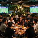 Viewing live sports while discussing tỷ lệ kèo nhà cái among friends at a lively outdoor sports bar.