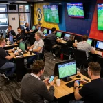 Watch live sports on multiple screens while placing bets at https://cak-t.com/, a vibrant sports betting venue atmosphere.