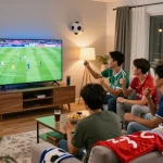 Friends enjoying football match on Okwintv in vibrant living room.