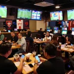 KÈO TRỰC TUYẾN passionately engaged by fans in a lively sports betting lounge, with multiple screens displaying exciting game action.